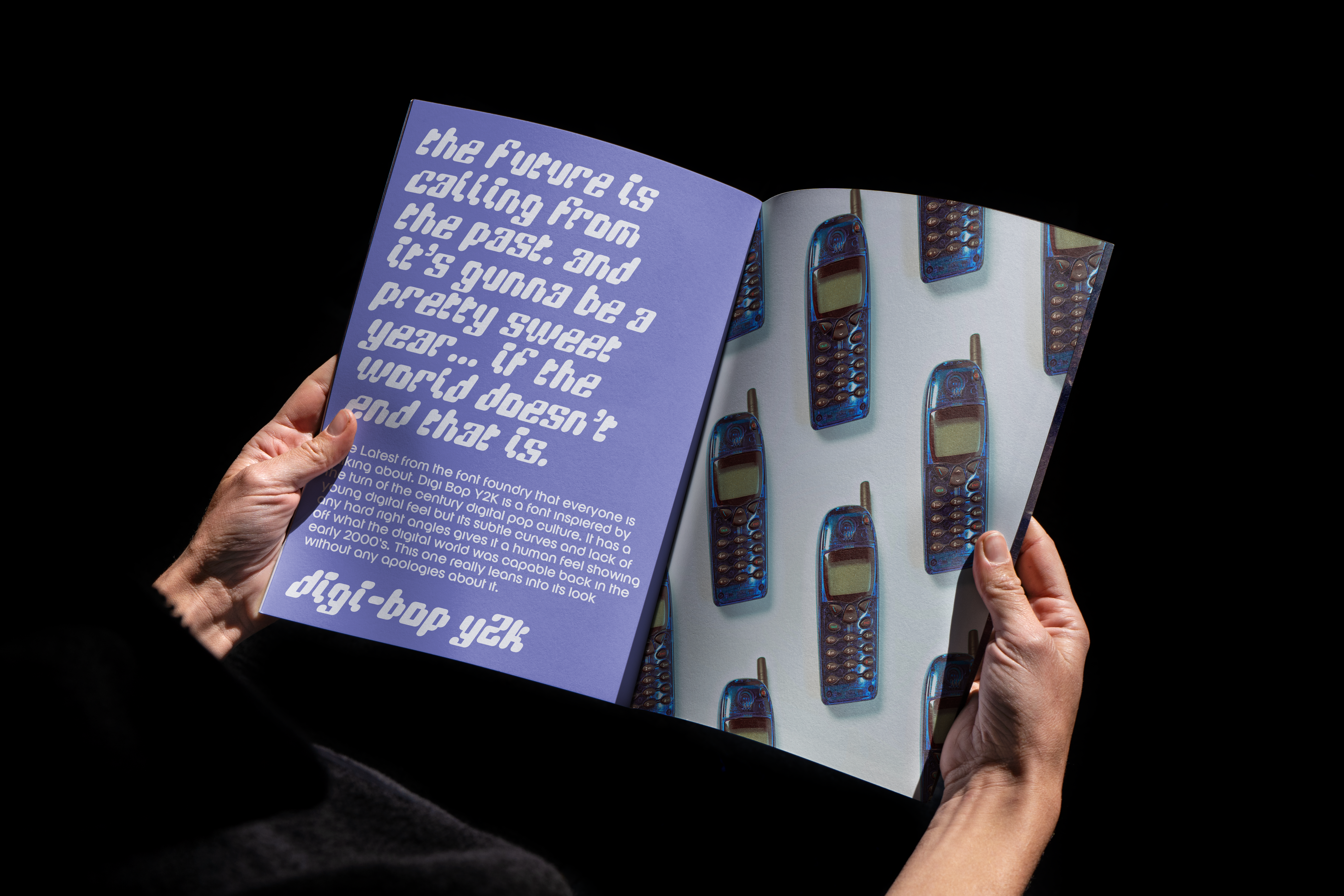 Designer holding open magazine with Y2K style font on purple page and vintage cellphone pattern. Perfect for graphics and typography inspiration.