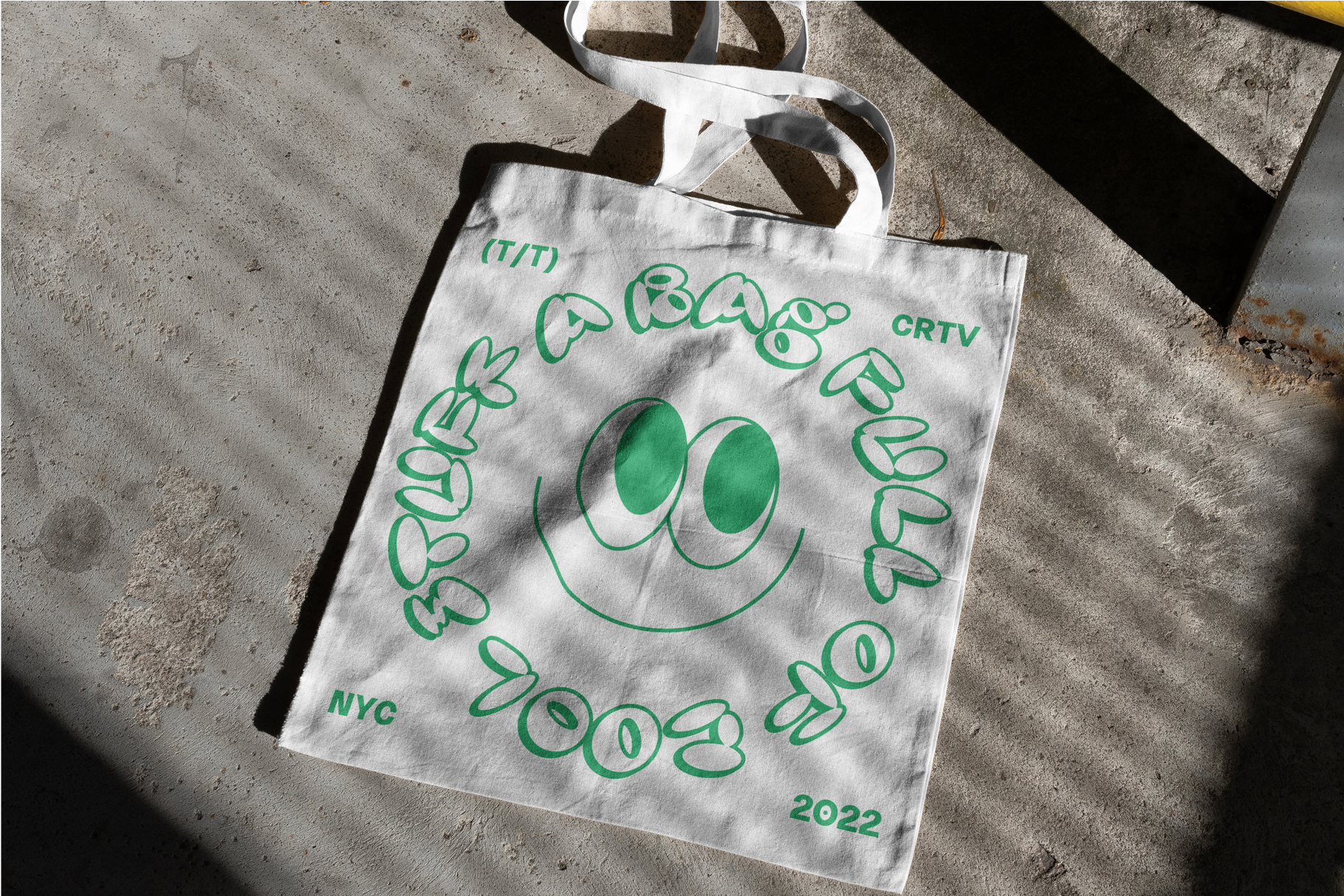 Tote bag mockup with retro green text and smiley face design on concrete background. Ideal for graphic designers and digital assets, NYC 2022 theme.