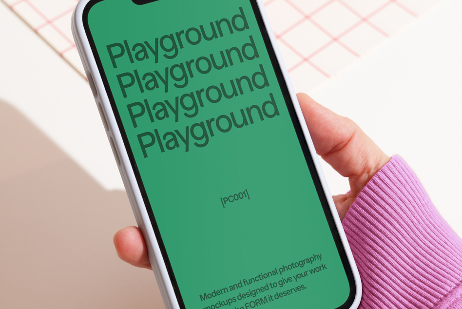 White iPhone with green screen in blue-sleeved hand over pink grid background