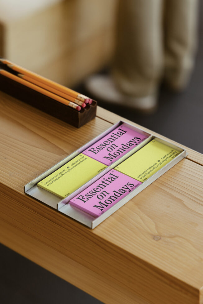 Essential on Mondays cards in tray on wooden desk with pencils nearby. Perfect for workspace organization mockup templates and stationery design displays.