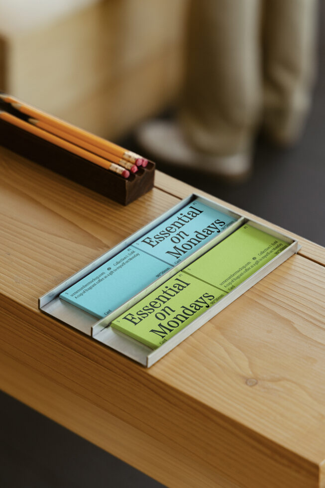 Wooden desk with pencils in holder and colorful note cards with Essential on Mondays text in modern font. Ideal for graphic design. Office decor.