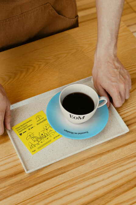 Barista serves coffee on a tray with a blue saucer and a design card. Keywords: Mockup, Coffee, Design, Tray, Card, Saucer, Barista, Photography.