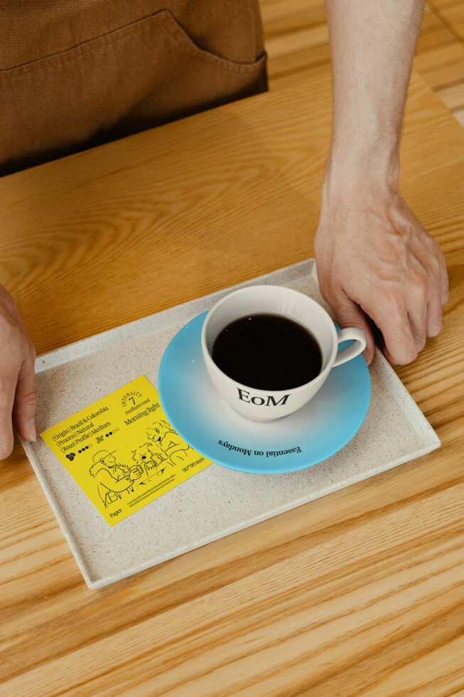 Barista serves coffee on a tray with a blue saucer and a design card. Keywords: Mockup, Coffee, Design, Tray, Card, Saucer, Barista, Photography.
