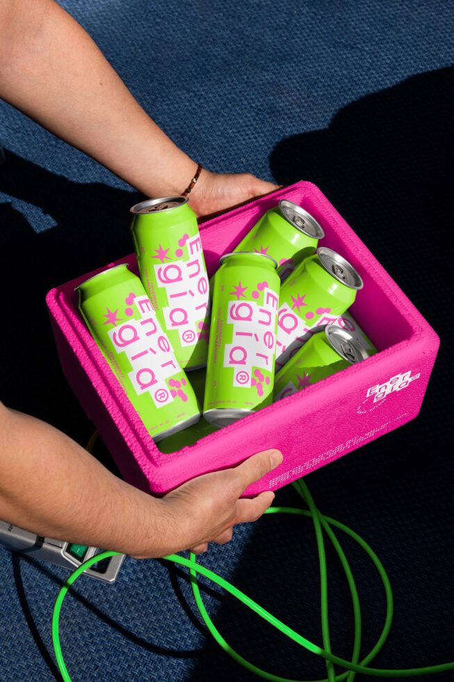 A person holds a pink box containing vibrant green energy drink cans with bold text; suitable for product mockups; ideal for graphic designers.