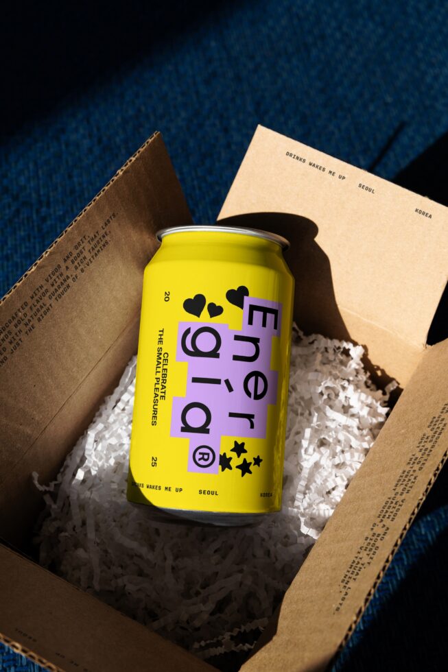 Yellow energy drink can with modern graphic design in a cardboard box on blue background. Perfect for mockup projects and branding templates.