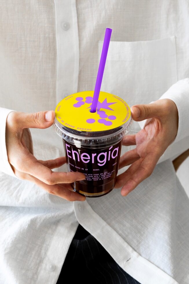 Person holding a beverage cup labeled Energia with vibrant purple straw and yellow lid. Mockup ideal for branding, packaging design, creative projects.