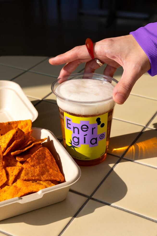 Hand reaching for a drink in a plastic cup with Energia label beside tortilla chips on a tiled table. Perfect for packaging and branding mockups.