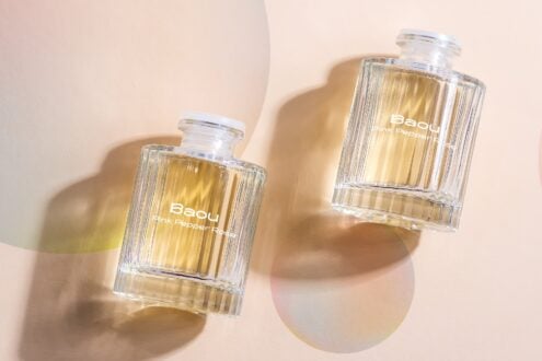 Two clear glass perfume bottles with golden liquid casting shadows on beige