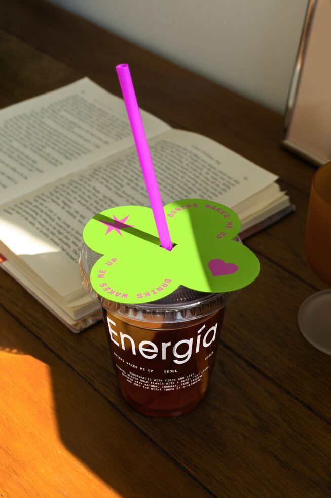 Cup of iced coffee with vibrant green lid and purple straw on wooden table next to open book. Ideal mockup for branding design packaging.