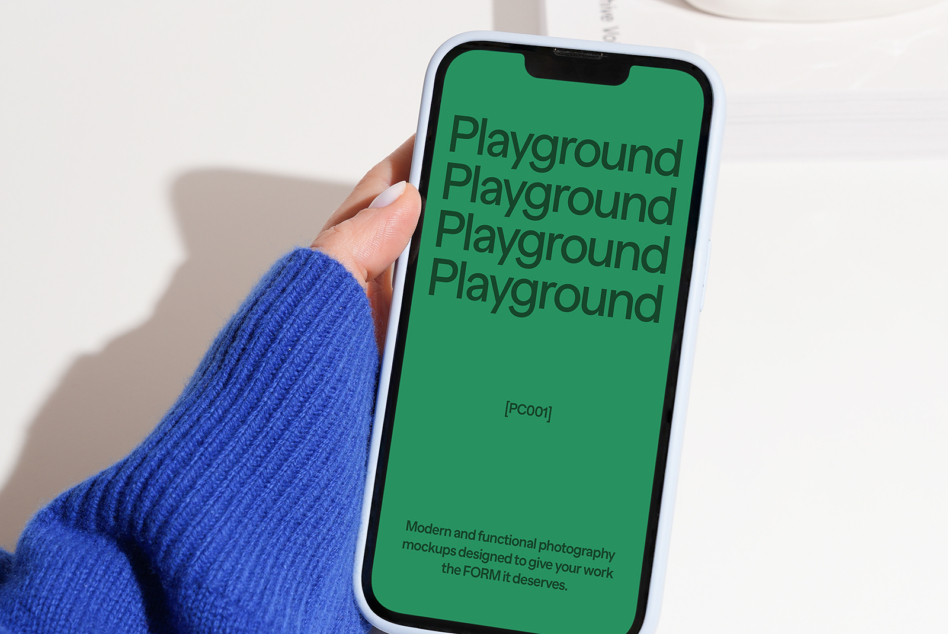 White iPhone with green screen showing Playground text on blue sweater sleeve