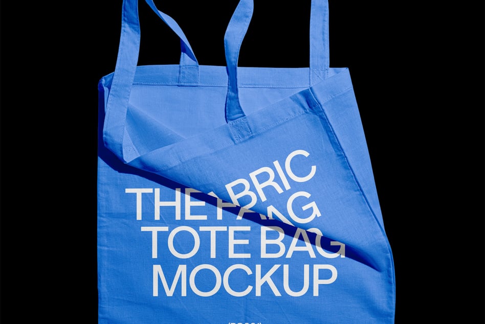 Blue fabric tote bag mockup with white text photographed against dark black background