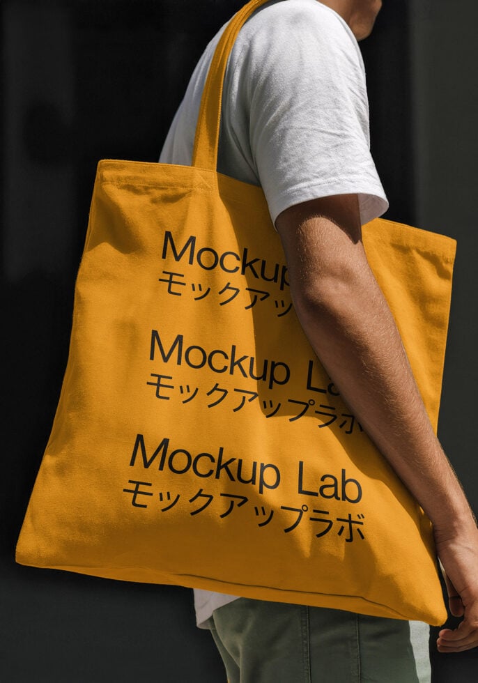 Yellow tote bag mockup with Japanese text held by person in white shirt. Ideal for showcasing branding designs. Perfect for graphic designers and mockups.