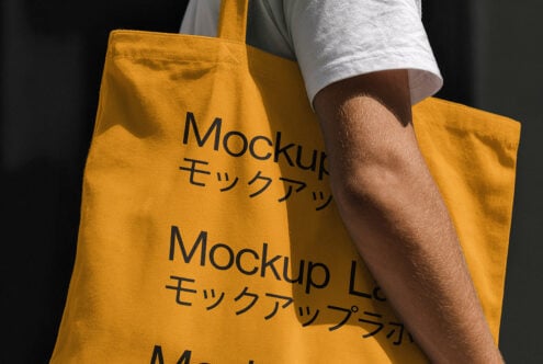 Yellow tote bag mockup with Japanese text carried by person in white shirt. Ideal for product presentation in graphic design templates.