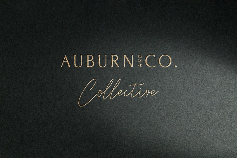 Auburn Land Co Collective brand text in gold lettering on dark textured background
