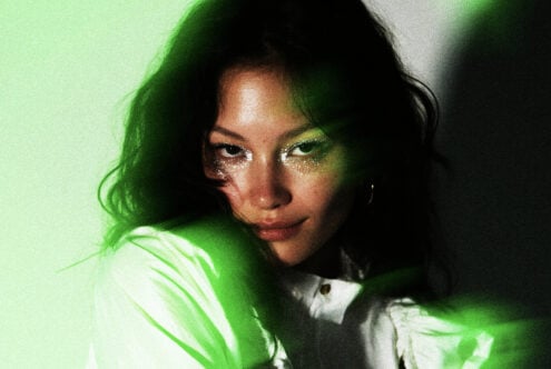 Woman with glittery eye makeup looking down with bright green light wash