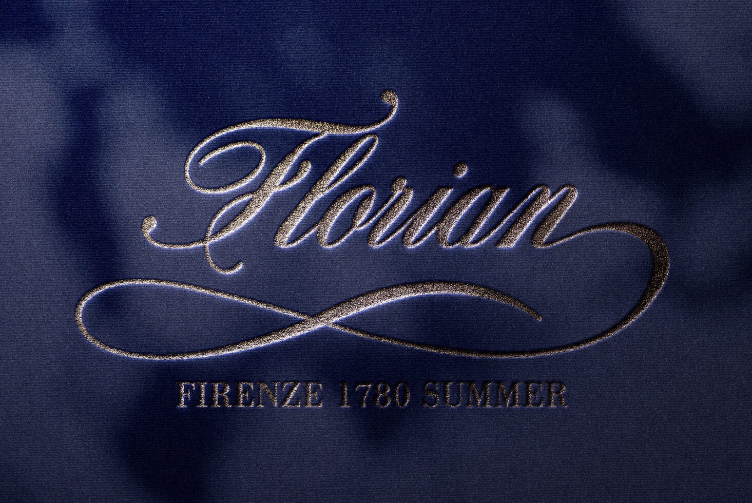 Ornate italic text with decorative underline in gold foil on blue fabric