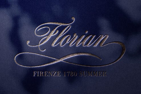 Ornate italic text with decorative underline in gold foil on blue fabric