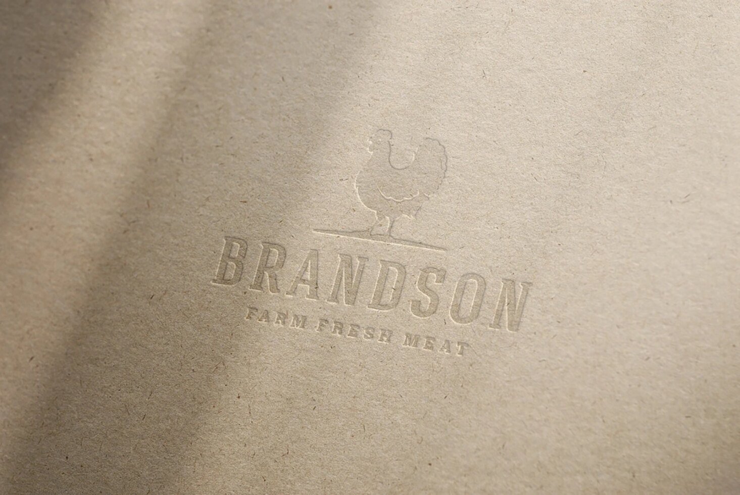 Mockup of embossed logo on textured paper featuring a chicken silhouette above the text Brandson Farm Fresh Meat. Ideal for branding design projects.