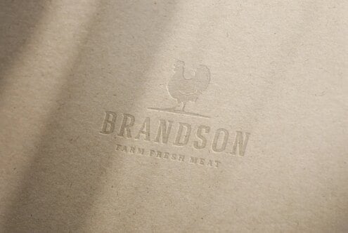 Mockup of embossed logo on textured paper featuring a chicken silhouette above the text Brandson Farm Fresh Meat. Ideal for branding design projects.