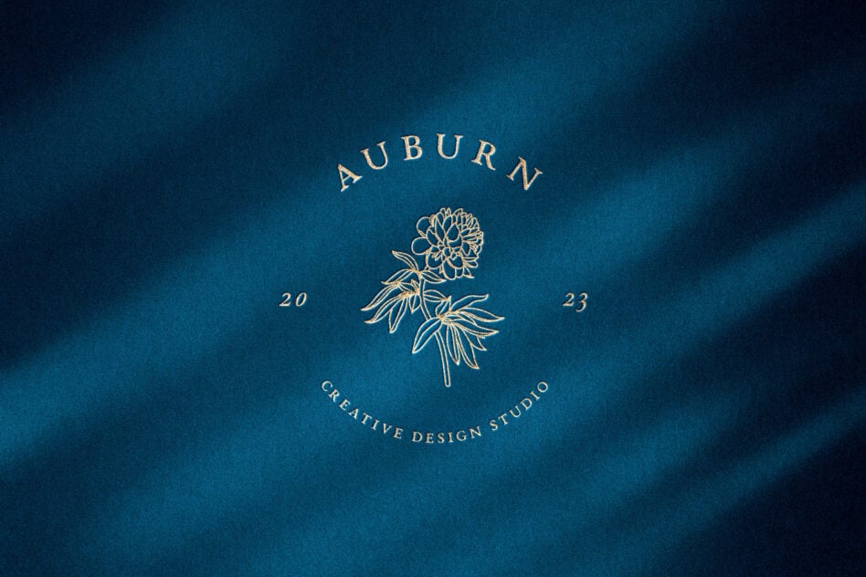 Auburn Creative Design Studio circular badge with peony flower illustration in gold on teal