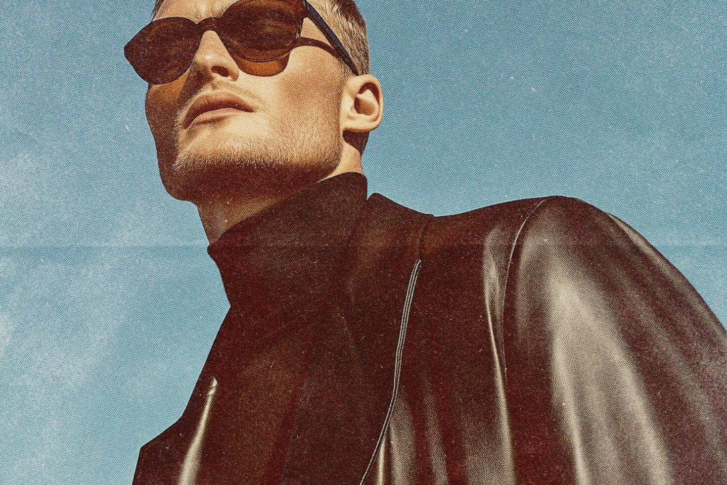 Man in brown leather jacket wearing oversized sunglasses against blue sky