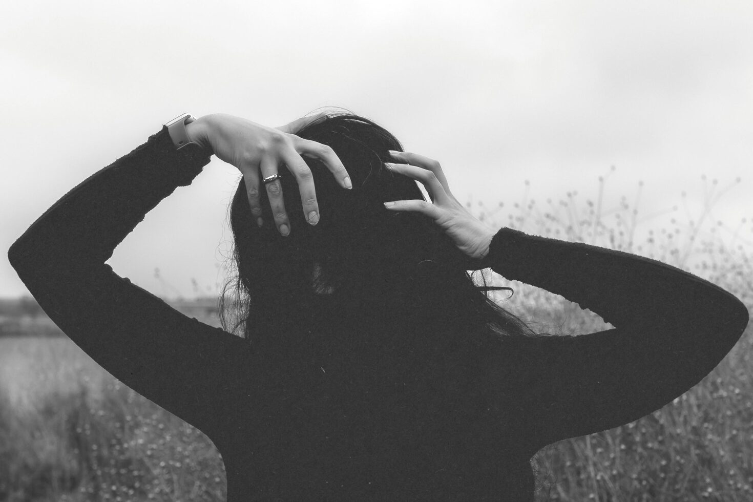 Black and white photo of a person with hands in hair, outdoor setting, wearing a watch and ring. Suitable for use in mockups or graphic design projects.