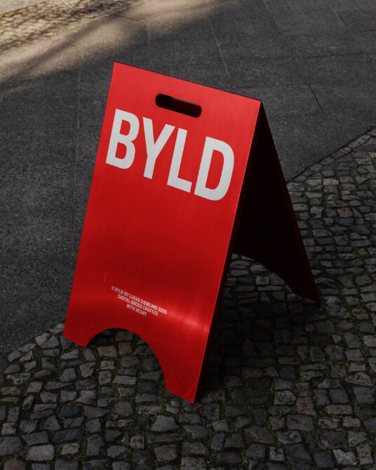 Red A-frame street sign with white BYLD lettering on brick