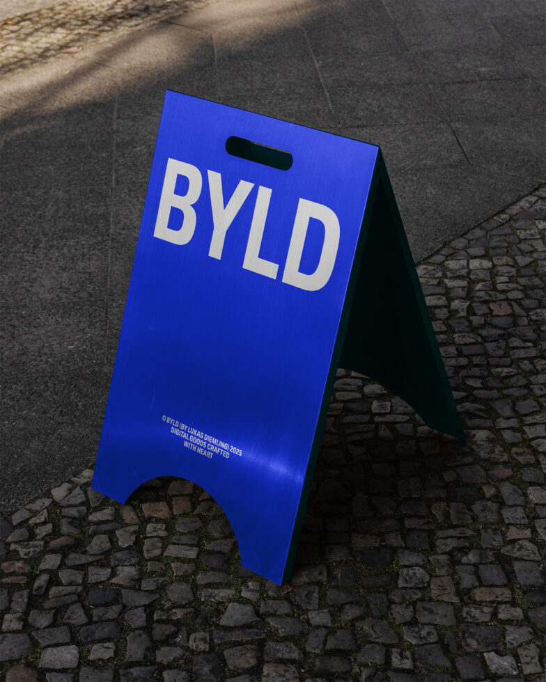 A blue metal display board with the text BYLD stands on a cobblestone street mockup signage template for designers advertising outdoor branding.