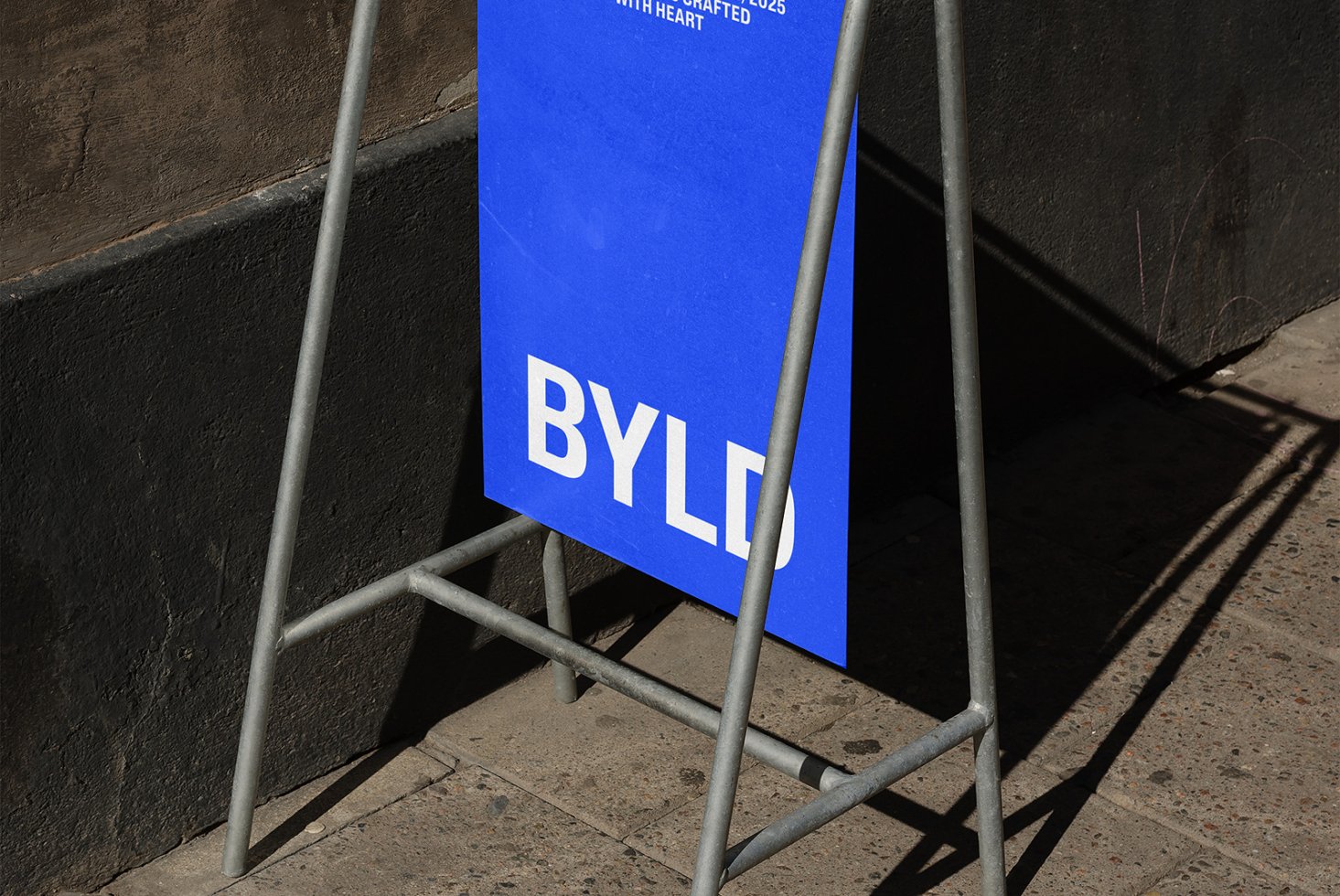 Blue signage poster mockup on a metal stand against a dark wall perfect for showcasing branding graphics or templates to creative designers