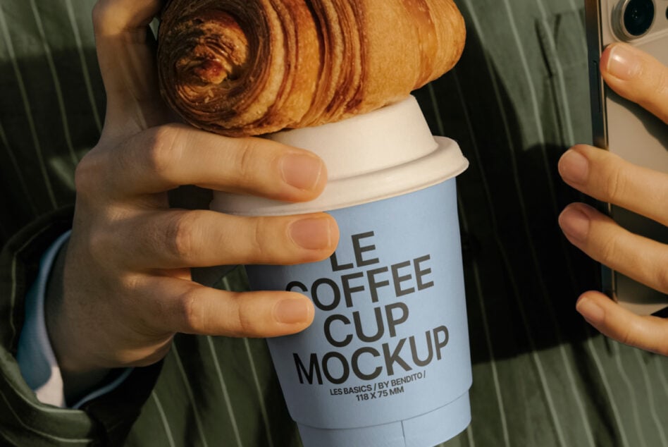 Croissant resting on white coffee cup mockup in person's hands outdoors