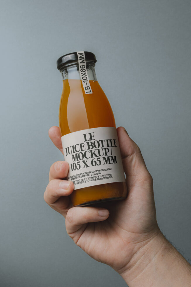 Hand holding juice bottle mockup against gray background, showcasing label design. Keywords: mockup, bottle, design, template, graphic, packaging.