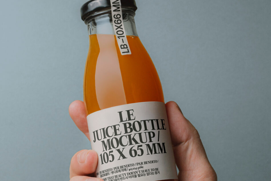 Hand holding amber glass juice bottle with white label against soft blue wall
