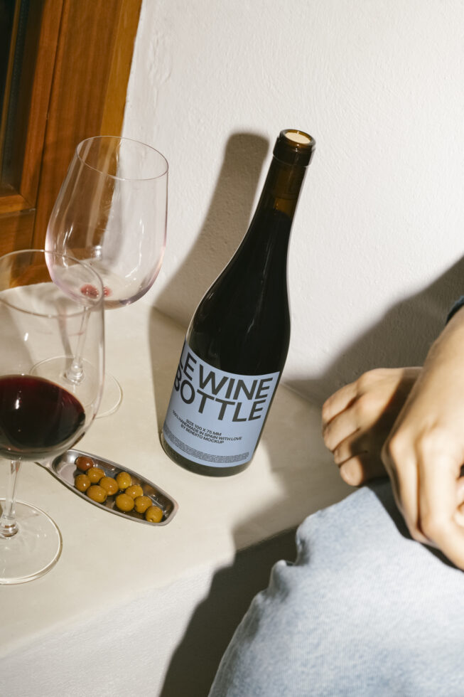Wine bottle mockup on white surface with two wine glasses and olives nearby suitable for showcasing label designs for designers seeking digital assets.