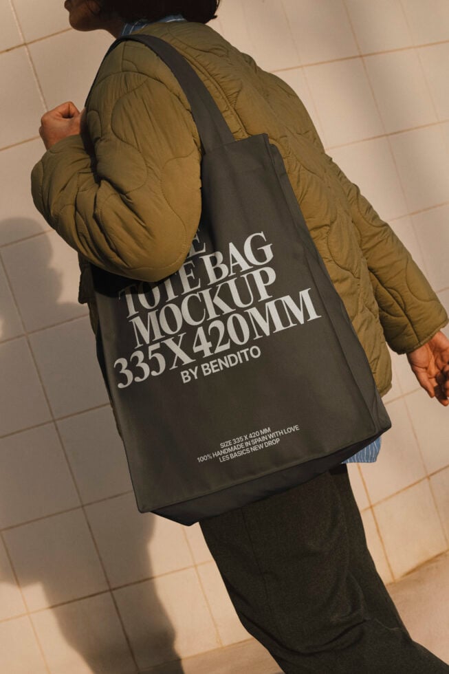 Tote bag mockup featuring a person wearing a green jacket. The bag displays text for a minimalist design. Ideal for designers creating branding concepts.