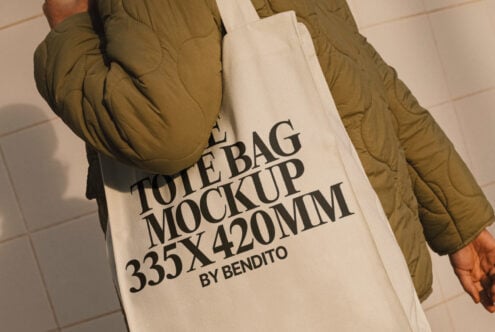 Canvas tote bag mockup held by a person in an olive jacket showcasing bold black typography 335x420mm ideal for designers mockups branding graphics.