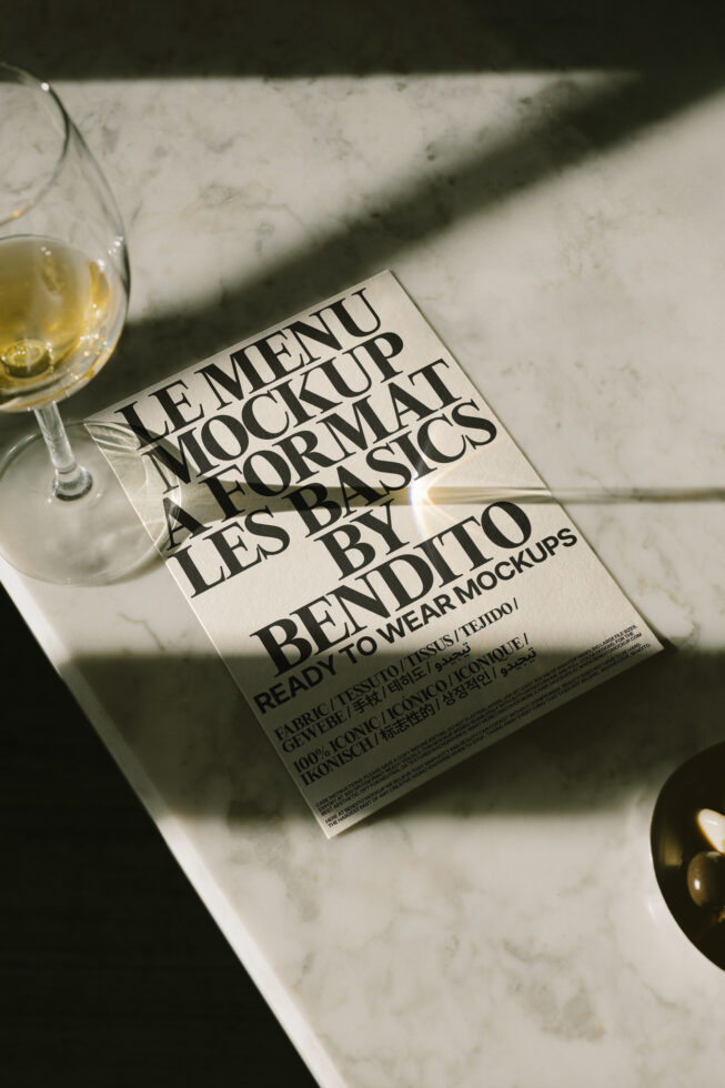 Mockup of a menu with elegant typography on a marble table beside a glass of white wine. Ideal for designers seeking high-quality mockups, graphics.