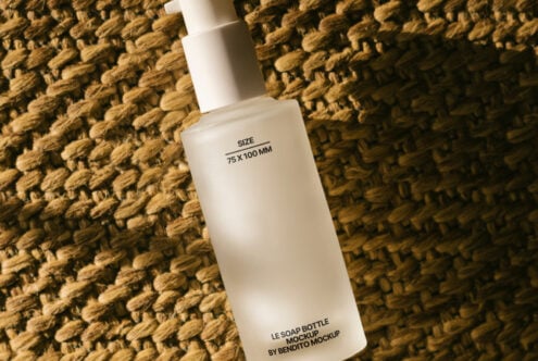 Frosted soap bottle mockup with pump, placed on textured woven surface, ideal for showcasing skincare product designs and packaging concepts for designers.