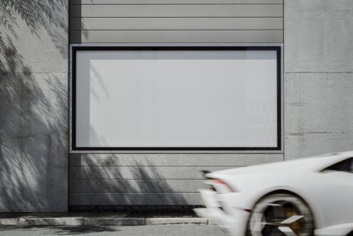 Blank outdoor billboard mockup on concrete wall with blurred white sports car passing by. Ideal for showcasing design. Keywords: Mockup, Billboard, Design.