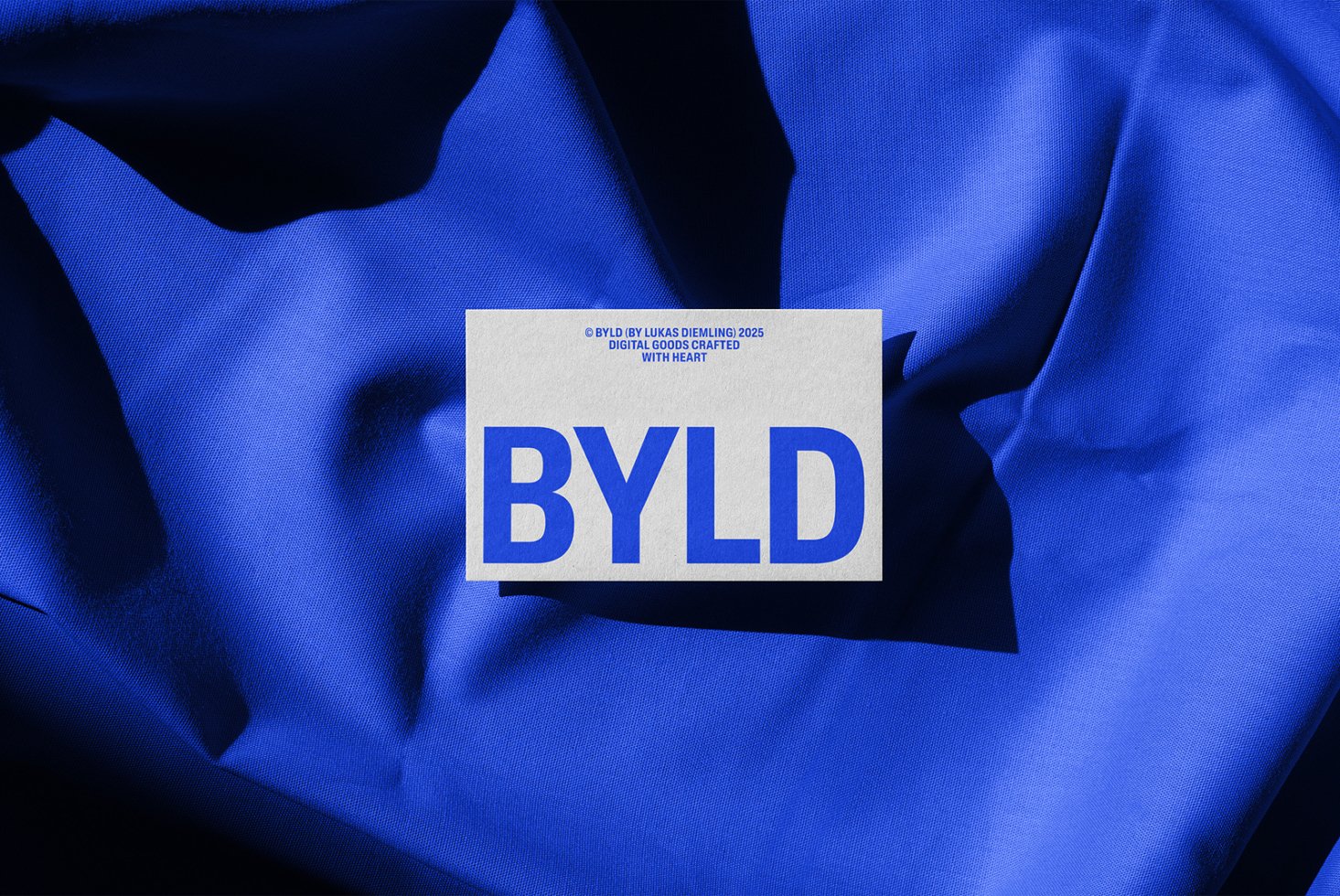 Blue fabric background with a white card displaying the word BYLD in bold blue font. Ideal for mockup, template, design assets.