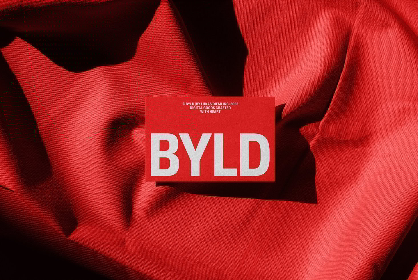 Red fabric backdrop with centered graphic mockup of a card labeled BYLD digital assets for designers bold typography cotton texture decorative design