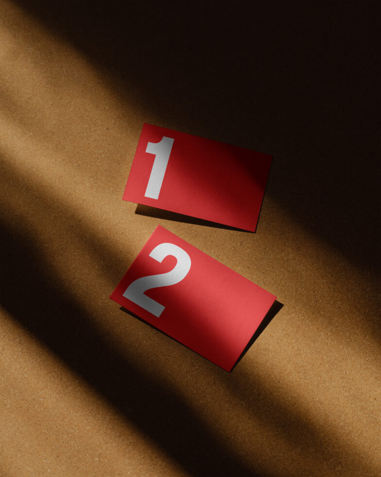 Red paper cards with numbers 1 and 2 on a brown surface in shadowing light. Ideal for graphic design mockups templates typography projects.