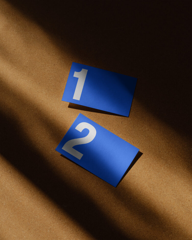 Blue paper cards with large white numbers one and two on a brown surface in shadow. Ideal for graphic design projects and template creation.