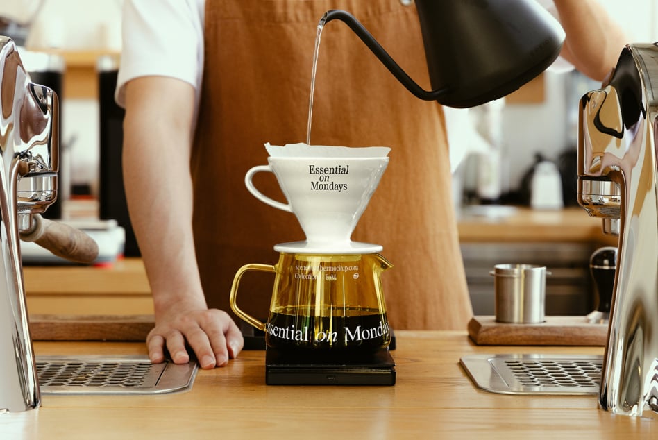 Person pouring from black gooseneck kettle into white ceramic dripper over glass carafe