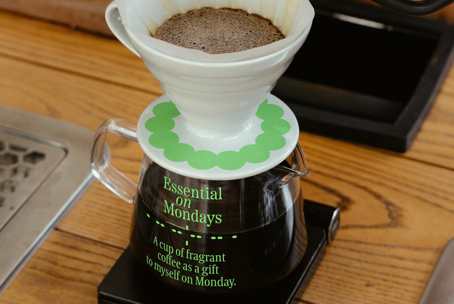 Pour-over coffee maker with wooden table background featuring text Essential on Mondays. Ideal for product mockups, coffee shop templates, design assets.