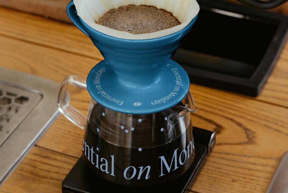 Close up of blue pour over dripper with grounds, glass carafe below catching brewed coffee