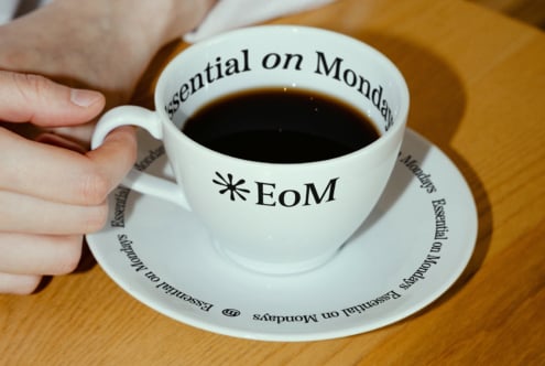 Coffee cup and saucer with Essential on Monday text design on wooden table. Ideal for branding mockups. Graphic design asset for designers.