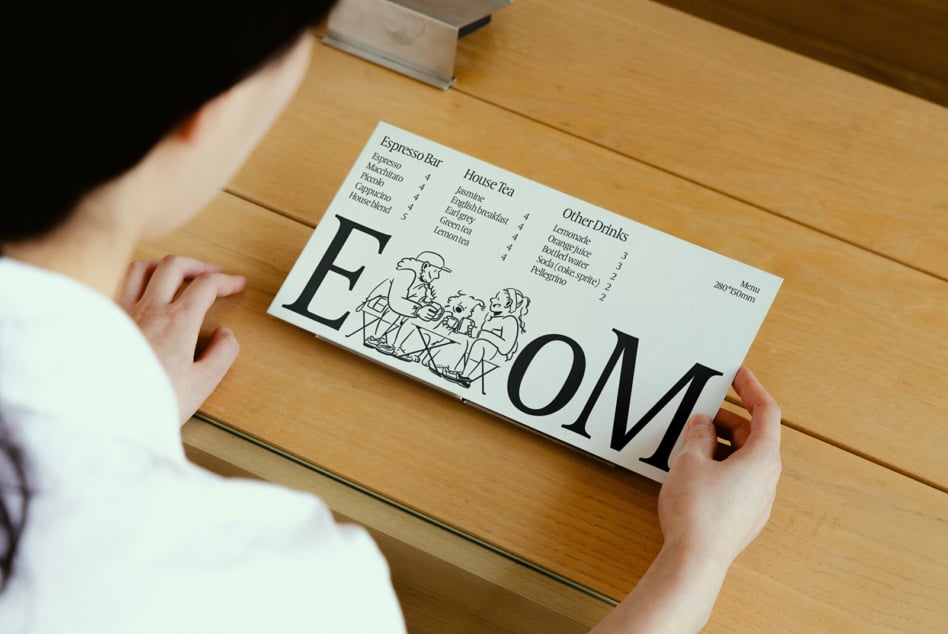 Cream colored cafe menu mockup with sketch people graphic, held in hands over wooden table