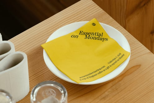Yellow napkin on a plate with Essential on Mondays text, ideal for branding mockups and design templates. Graphic asset for creative designers.