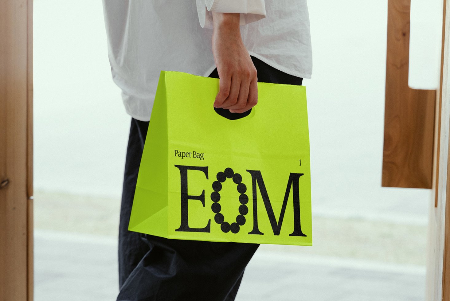 Person holding a vibrant green shopping bag with bold EOM text design. Perfect for branding mockups and packaging graphics. Designer resource.