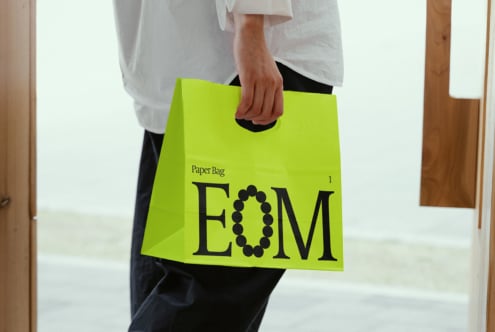 Person holding a vibrant green shopping bag with bold EOM text design. Perfect for branding mockups and packaging graphics. Designer resource.
